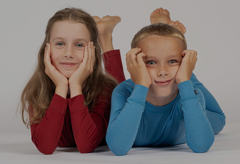 Twee kinderen, een meisje in een rood shirt en een jongen in een blauw shirt, liggend op een grijze achtergrond met hun voeten omhoog.