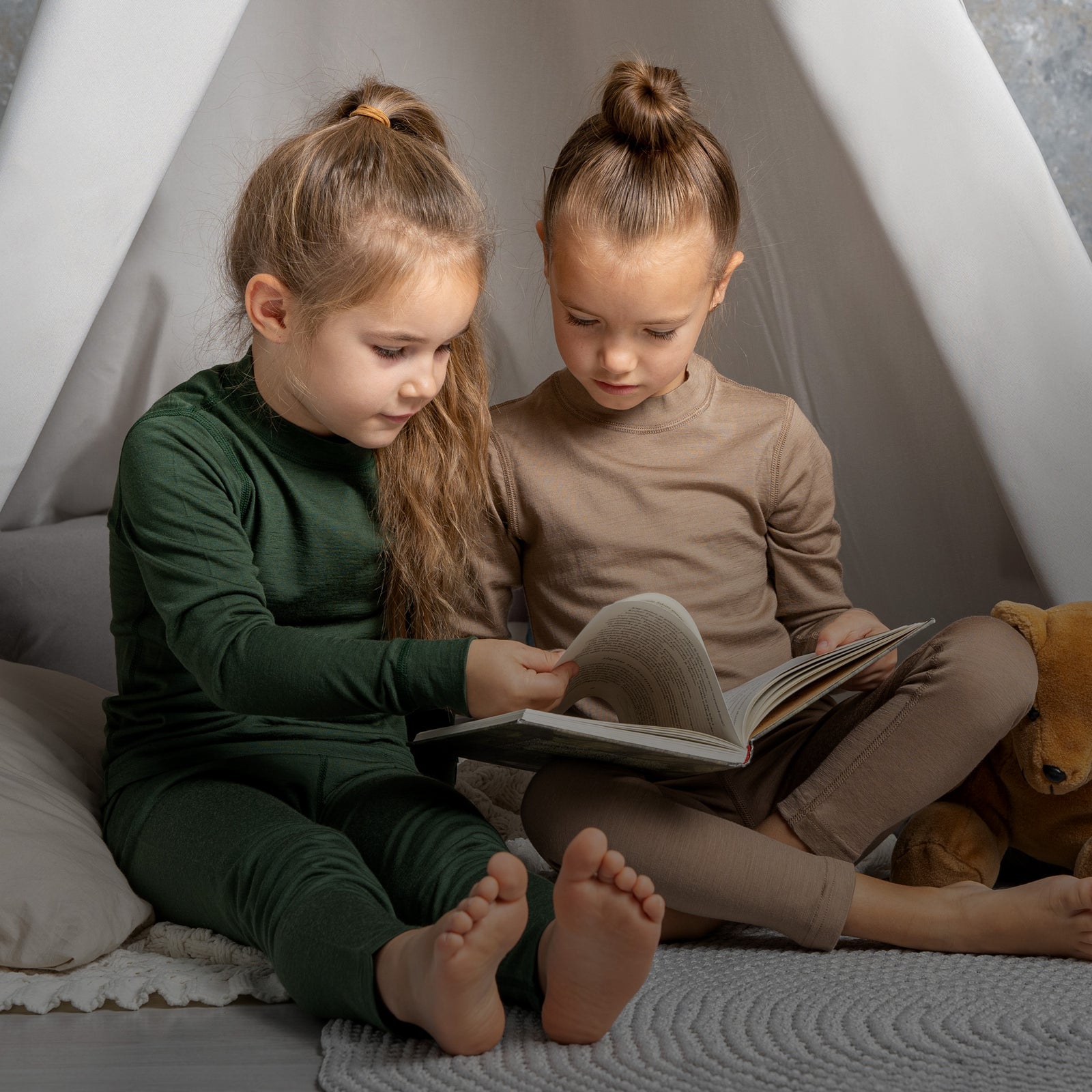 Twee kinderen zitten in een tipi en lezen een boek.