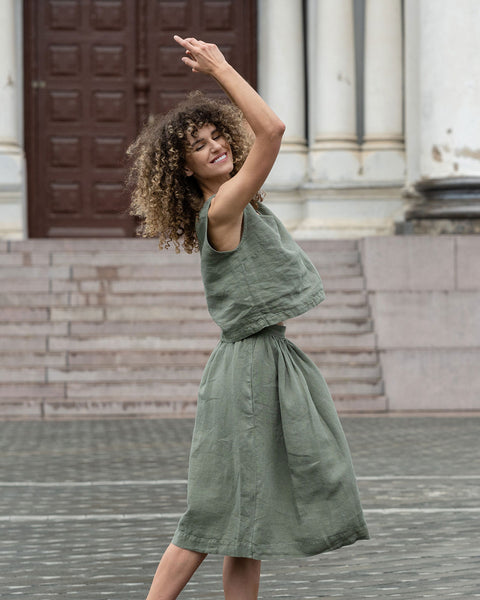 Vrouw met een krullend kapsel poseert in de stad, gekleed in een steen groene cropped top en een steen groene rok Sophia.